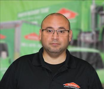 a man in a black shirt standing in front of a green SERVPRO truck