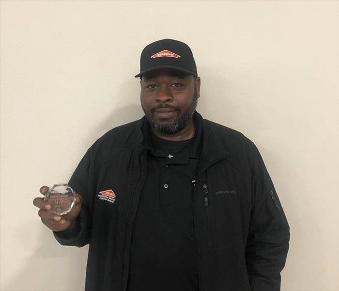 a man holding an award in front of a beige wall